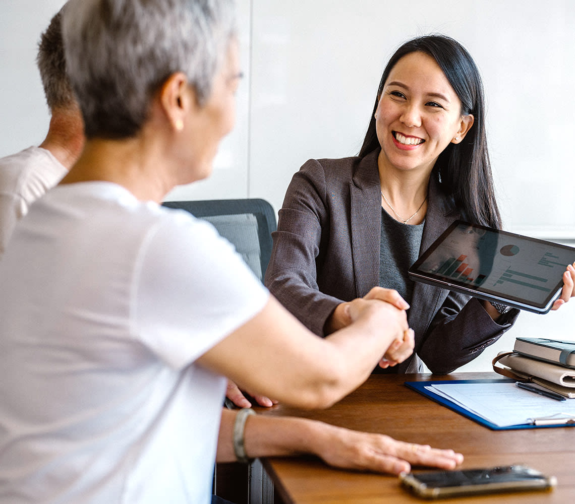Two women engage in a handshake at a table, representing a successful meeting or partnership in a business environment.
