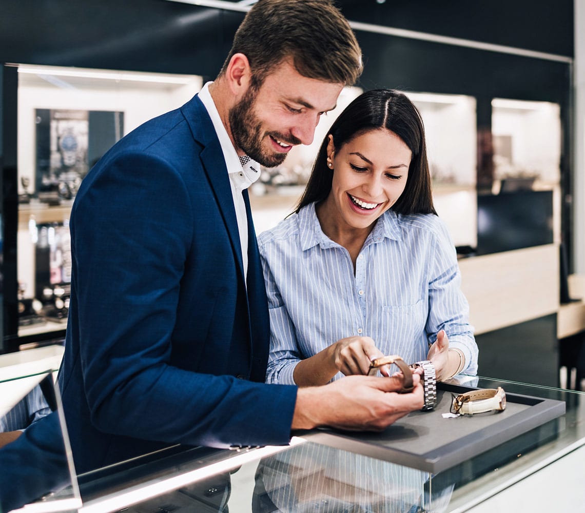 A couple inspects various watches in a jewelry store, reflecting their desire to choose the perfect timepiece together.