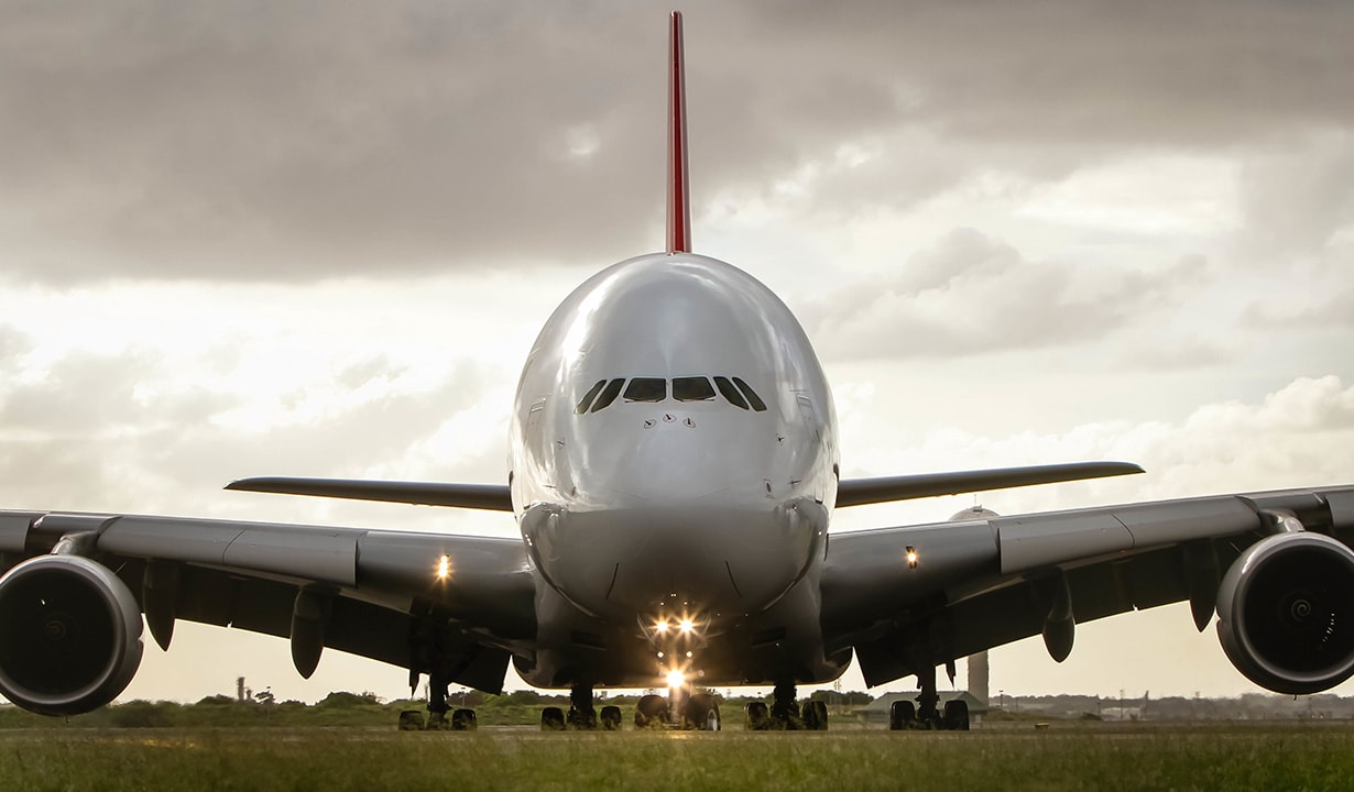 Un grande aereo commerciale visto dal davanti posizionato su una pista di decollo con un cielo nuvoloso sullo sfondo.