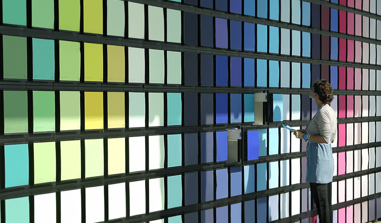 A woman stands thoughtfully in front of a vibrant wall displaying various color samples for selection.