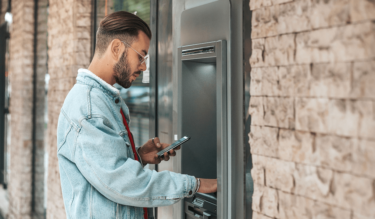 A man is using an ATM, engaged in a financial transaction in a busy city environment.