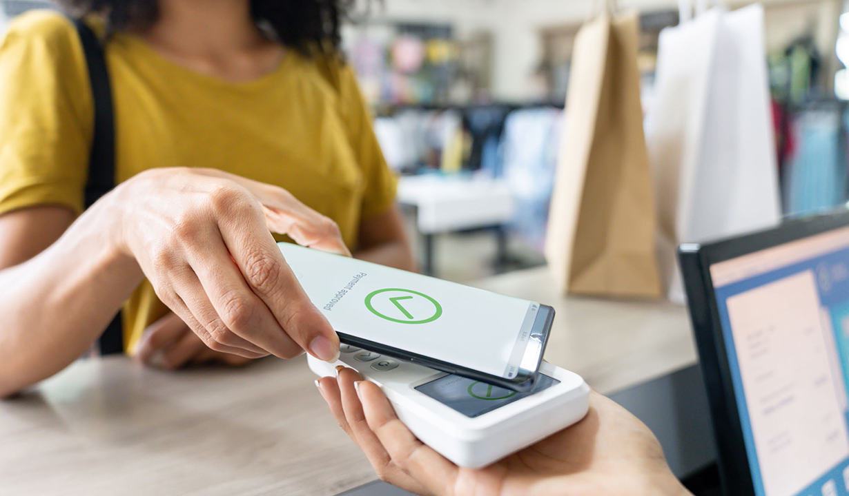 A woman making a mobile payment, holding her phone while completing a transaction at a store.