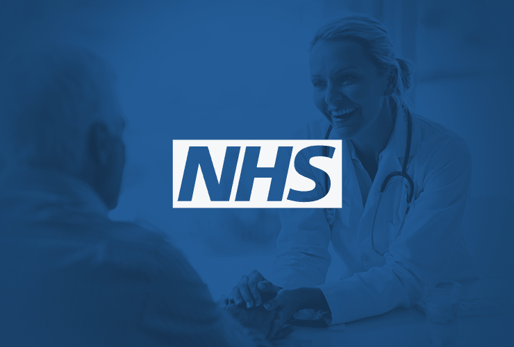 A doctor smiling at an elderly patient with an NHS logo in the foreground on a blue-tinted background.