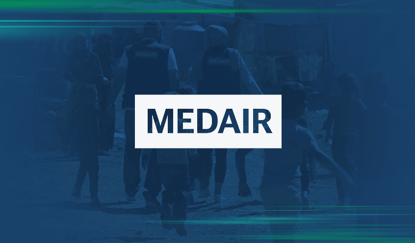 The image shows the logo of Medair, overlaid on a blurred background of a group of Medair workers provides essential support in remote areas.